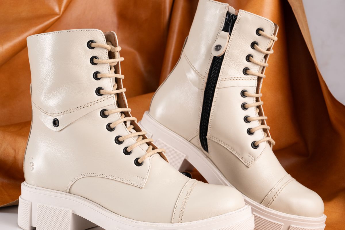 A pair of cream leather lace-up ankle boots against a tan leather backdrop