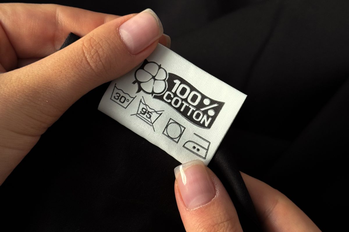 Hands holding the care and fibre label of a cotton garment