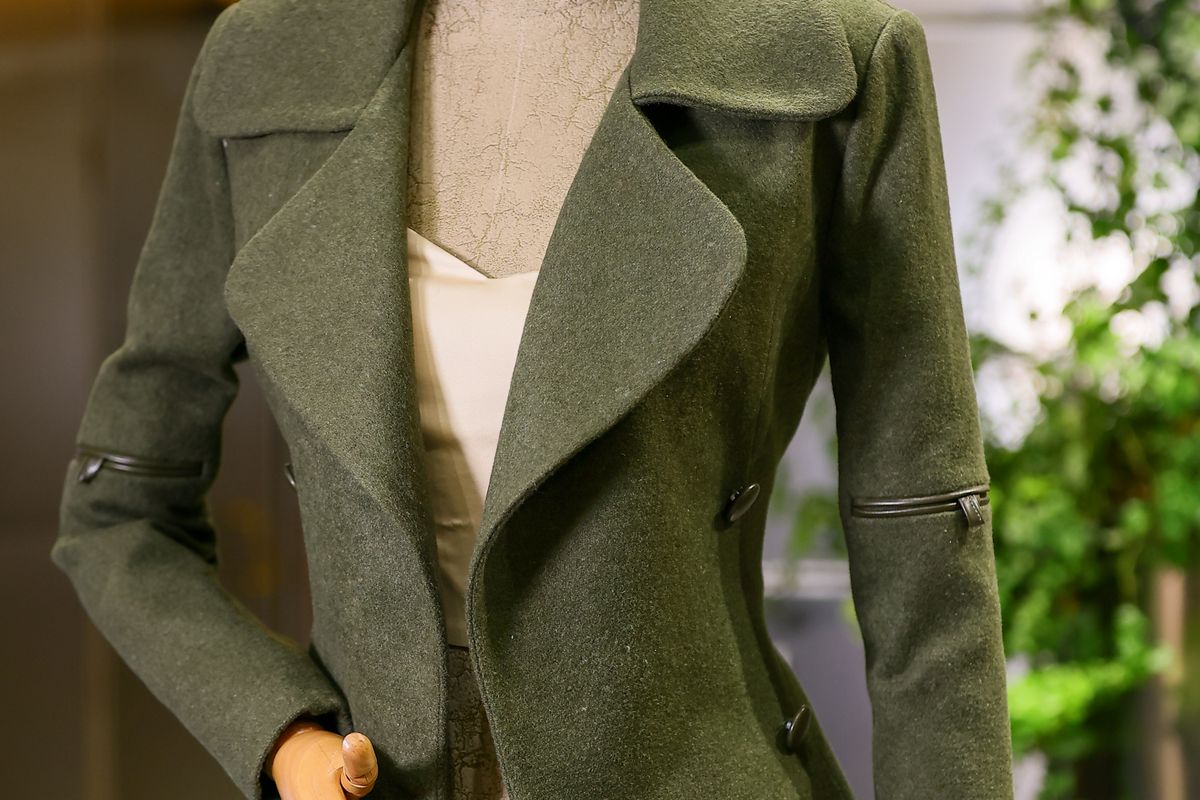 An olive-green wool coat fitted on a dress form, photographed from the front